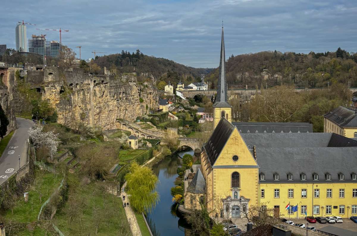 a photo of the Grund valley in Luxembourg City showing the Alzette river, Neumünster Abbey, and the Kirchberg skyline in the distance, Luxembourg, photo by Next Level of Travel