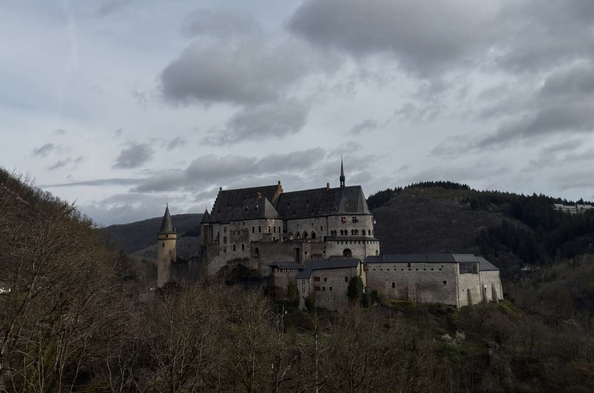 a photo of the Vianden Castle from afar, with the surrounding hills and forests visible in the background, Luxembourg, photo by Next Level of Travel