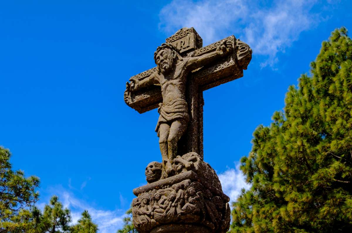 a detailed stone crucifix standing against a clear blue sky surrounded by Canary pine trees at Cruz de Tejeda, Gran Canaria, Canary Islands