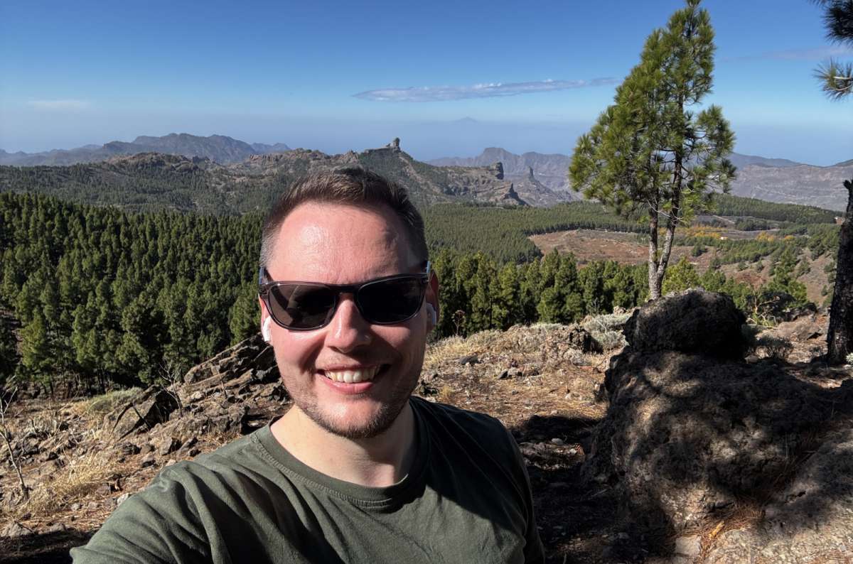 a photo of a tourist taking a selfie at Pico de las Nieves with Roque Nublo and pine forests visible in the background, Gran Canaria, Canary Islands, photo by Next Level of Travel
