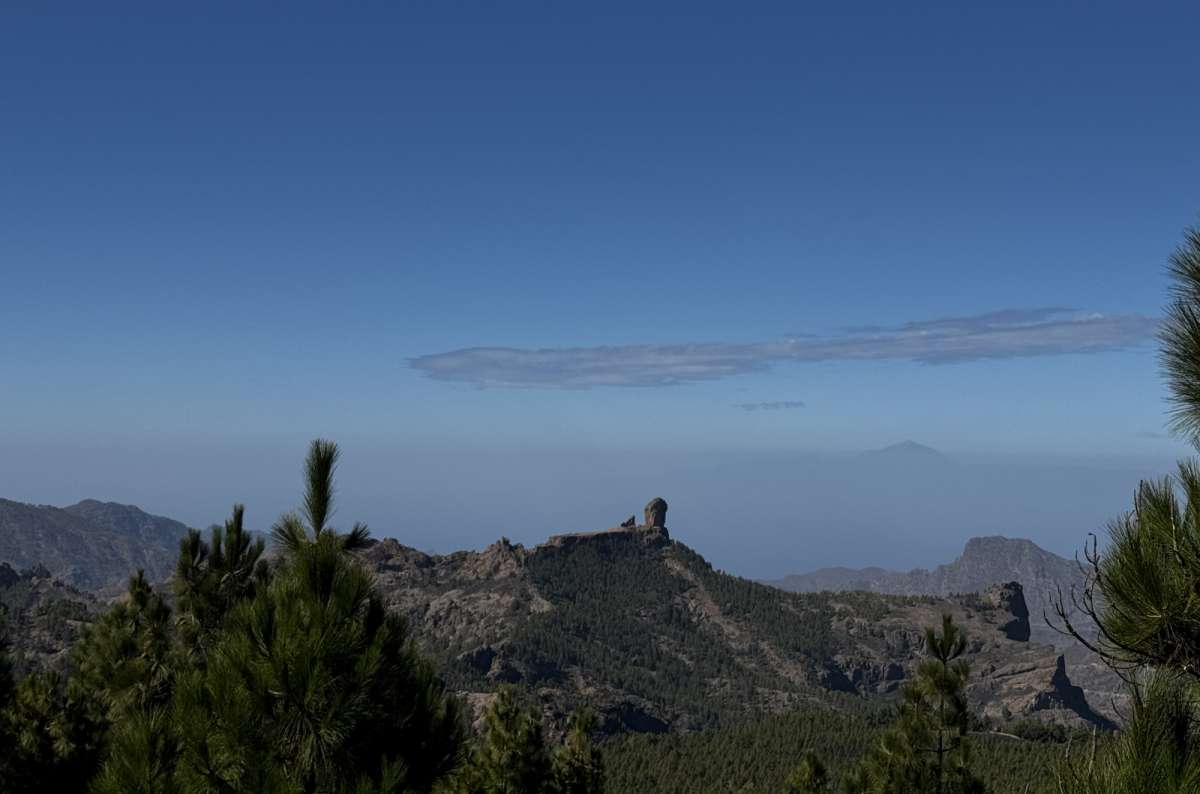 a photo of Roque Nublo above the pine forests with the silhouette of Mount Teide in Tenerife visible on the horizon, seen from Pico de las Nieves, Gran Canariphoto by Next Level of Travel