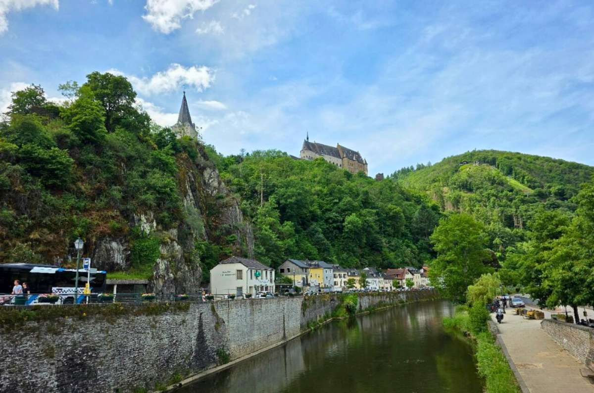 View of the Our River flowing through Vianden with Vianden Castle rising above the forested hillside, Luxembourg