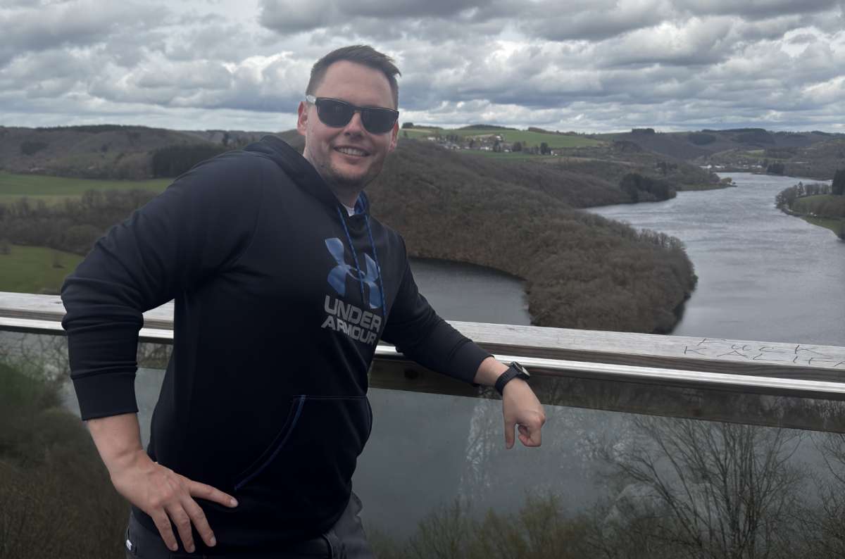 A tourist at a railing above the Upper Sûre lake and forested hills, Burfelt, Luxembourg, photo by Next Level of Travel 