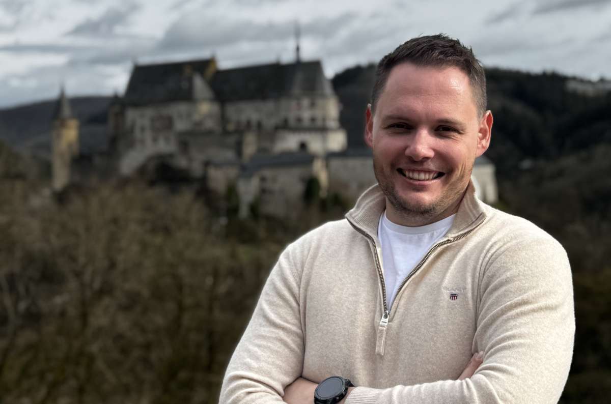 a photo of a tourist at a hillside viewpoint with Vianden Castle rising above the valley behind, Vianden, Luxembourg, photo by Next Level of Travel