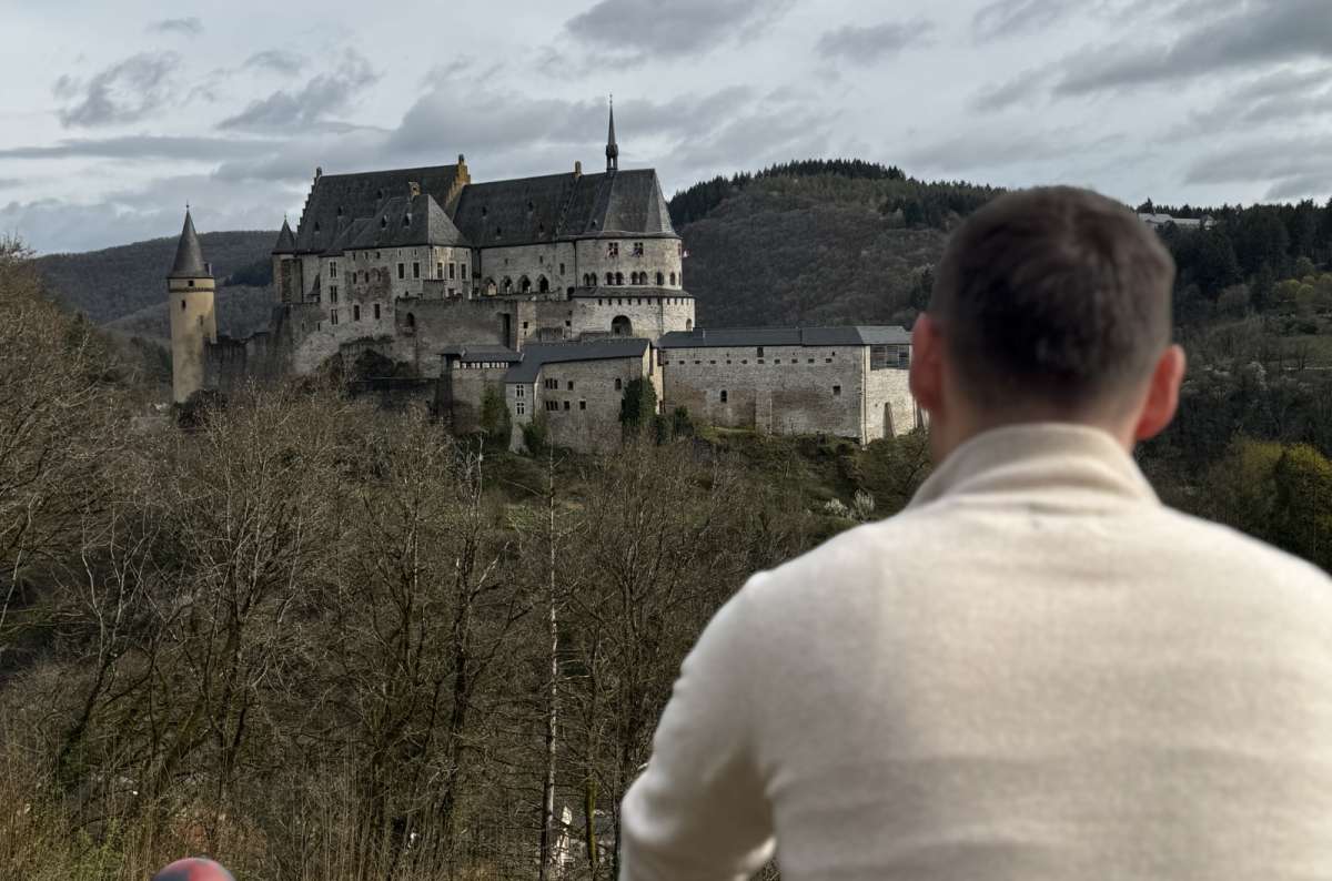 a photo of a tourist looking out at Vianden Castle from a hillside viewpoint, Vianden, Luxembourg, photo by Next Level of Travel