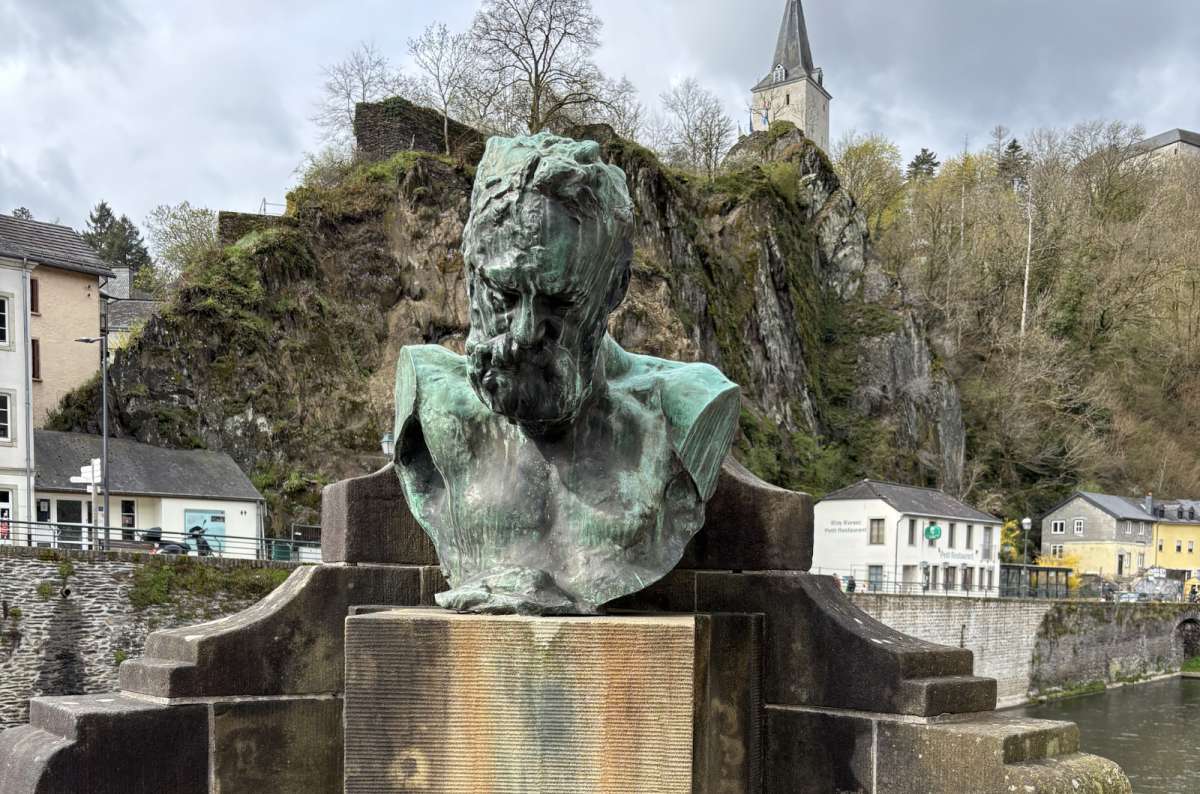 a photo of the bronze Victor Hugo bust with Vianden town and castle behind, Vianden, Luxembourg, photo by Next Level of Travel