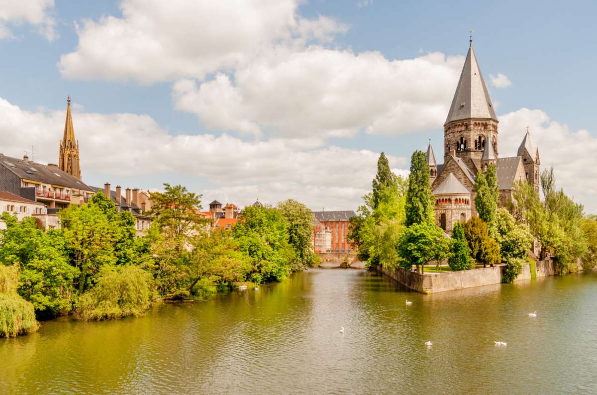 a photo of the Temple Neuf church on its green island in the Moselle river with swans on the water, Metz, France, photo by Next Level of Travel