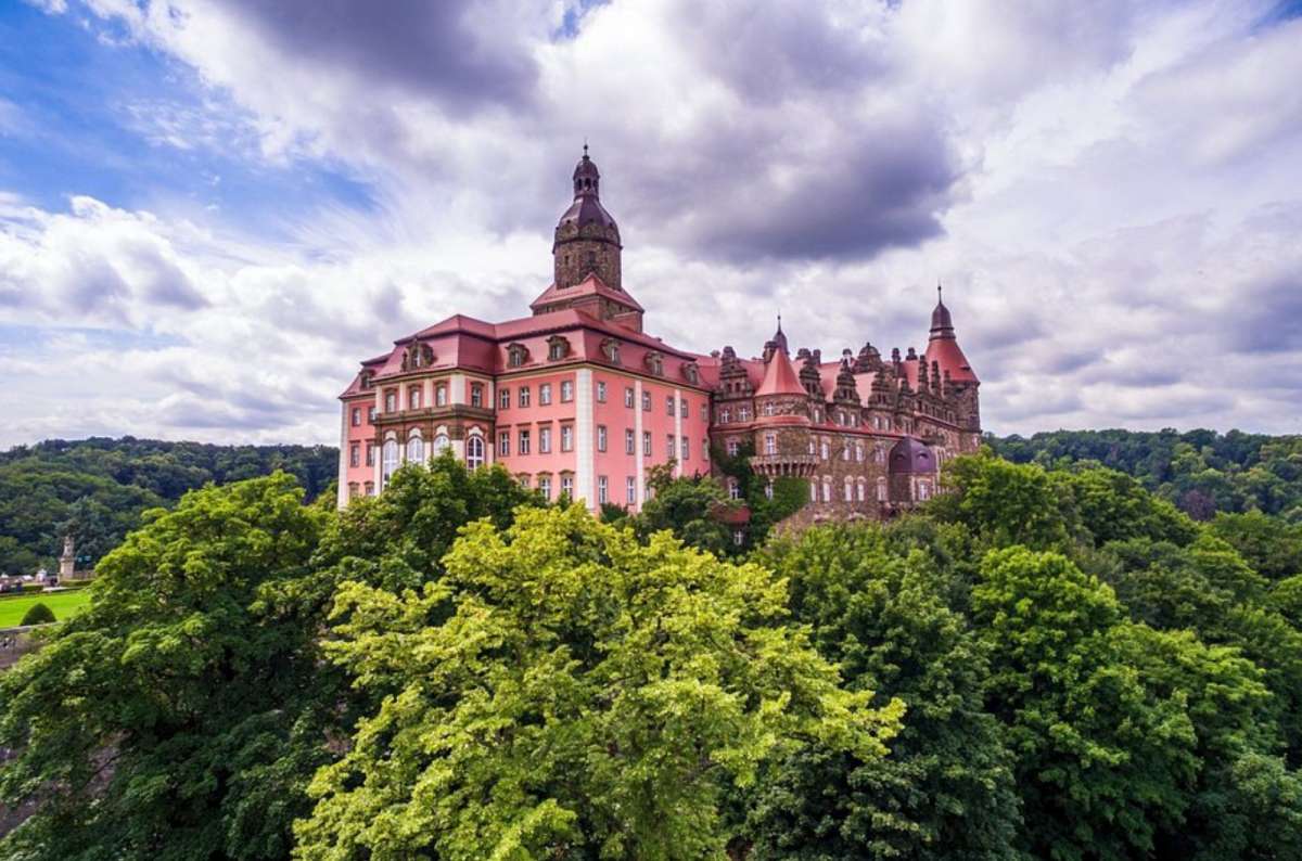 a photo of Ksiaz Castle from afar, showing the red castle surrounded by forests, Poland