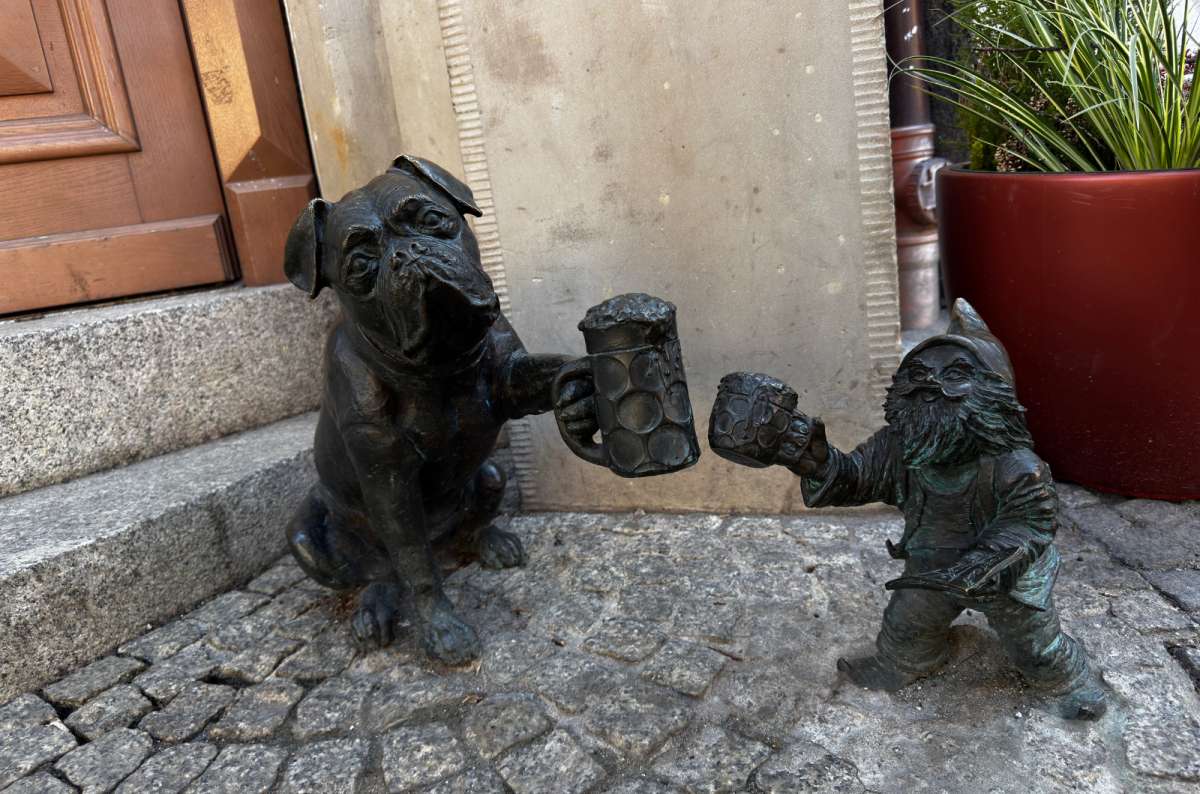 a photo of the dwarf miniature sculpture raising a glass with a sculpture of a dog, Poland, photo by Next Level of Travel