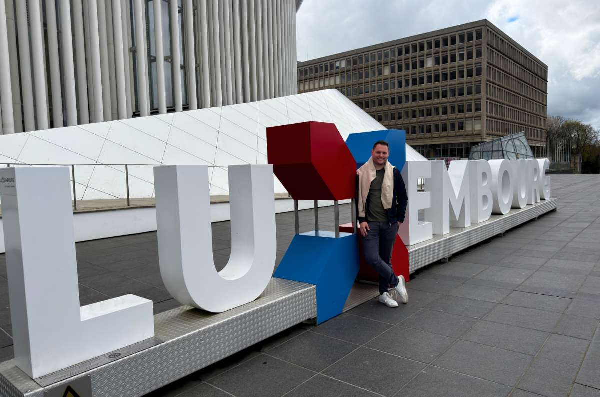 photo of a tourist standing by the giant Luxembourg letters sign in Kirchberg, Luxembourg City, photo by Next Level of Travel