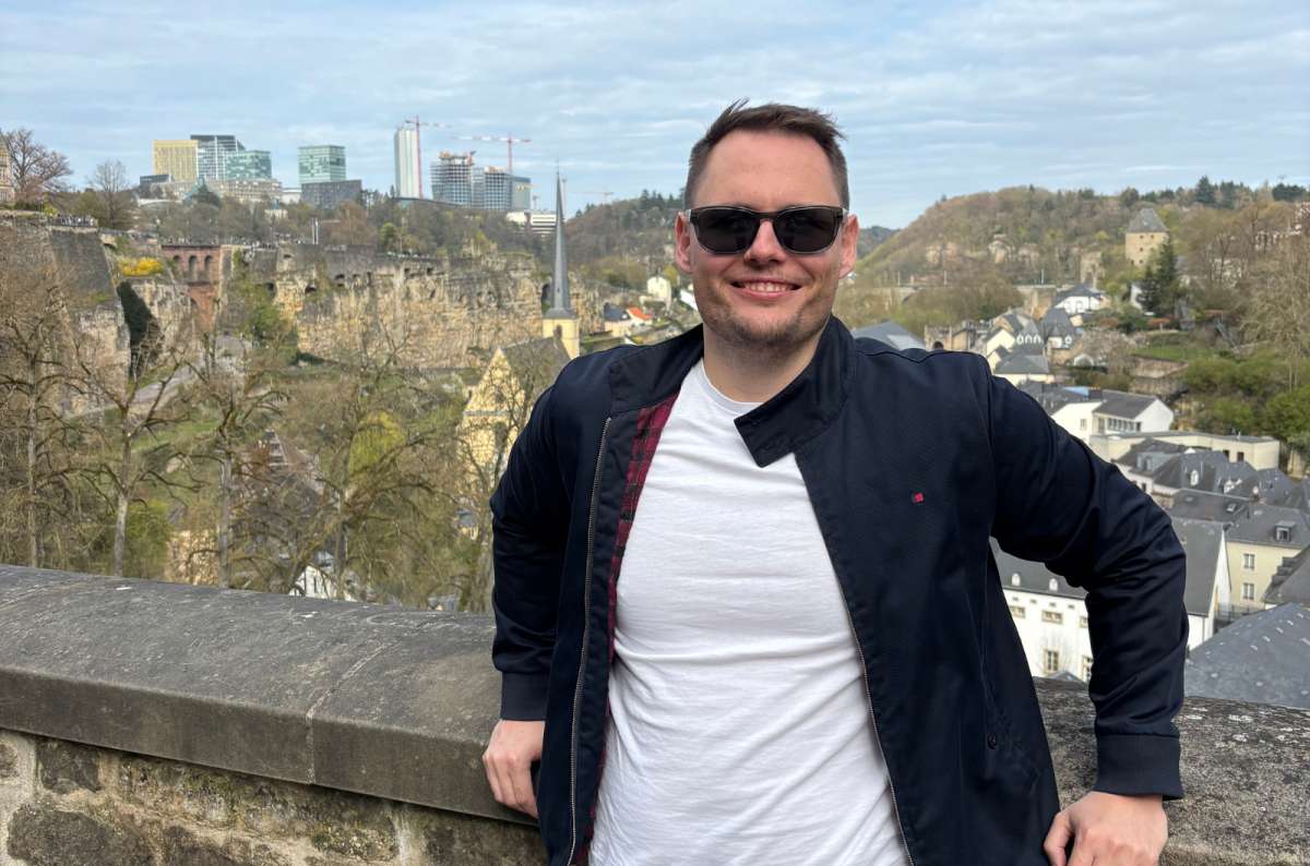 tourist standing on the Chemin de la Corniche with the Grund district and Kirchberg skyline behind him, Luxembourg City, photo by Next Level of Travel
