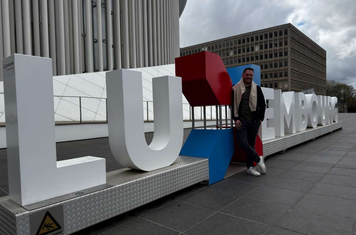 a tourist standing in front of the Luxembourg sign next to the Concert Hall of the Philharmony, Luxembourg, a photo by Next Level of Travel
