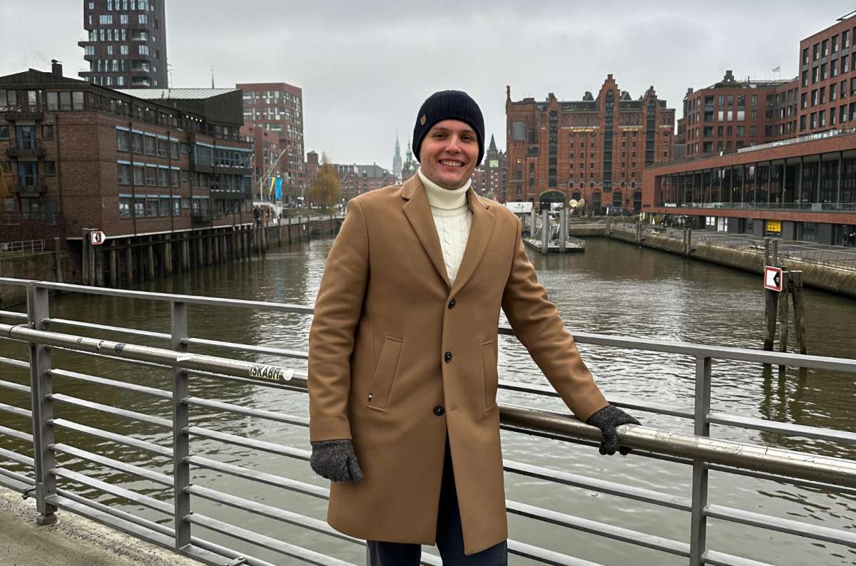 a photo of a tourist posing in front of a railing in HafenCity with the Elbe river visible in the background, Germany, photo by Next Level of Travel