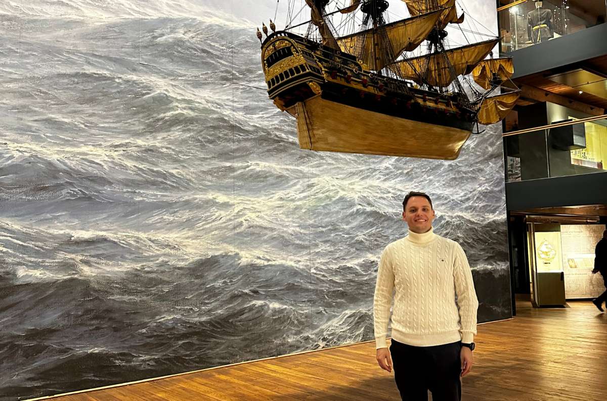 a photo of a tourist posing in front of the painting of the sea texture and a boat hung up in the air visible in the background, International Maritime Museum, Germany, photo by Next Level of Travel