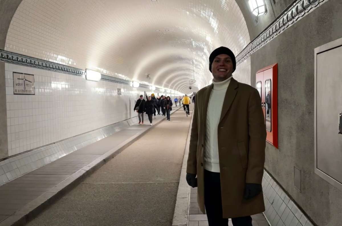 a photo of a tourist posing in the Old Elbe Tunnel with tourists walking in the background, Germany, photo by Next Level of Travel
