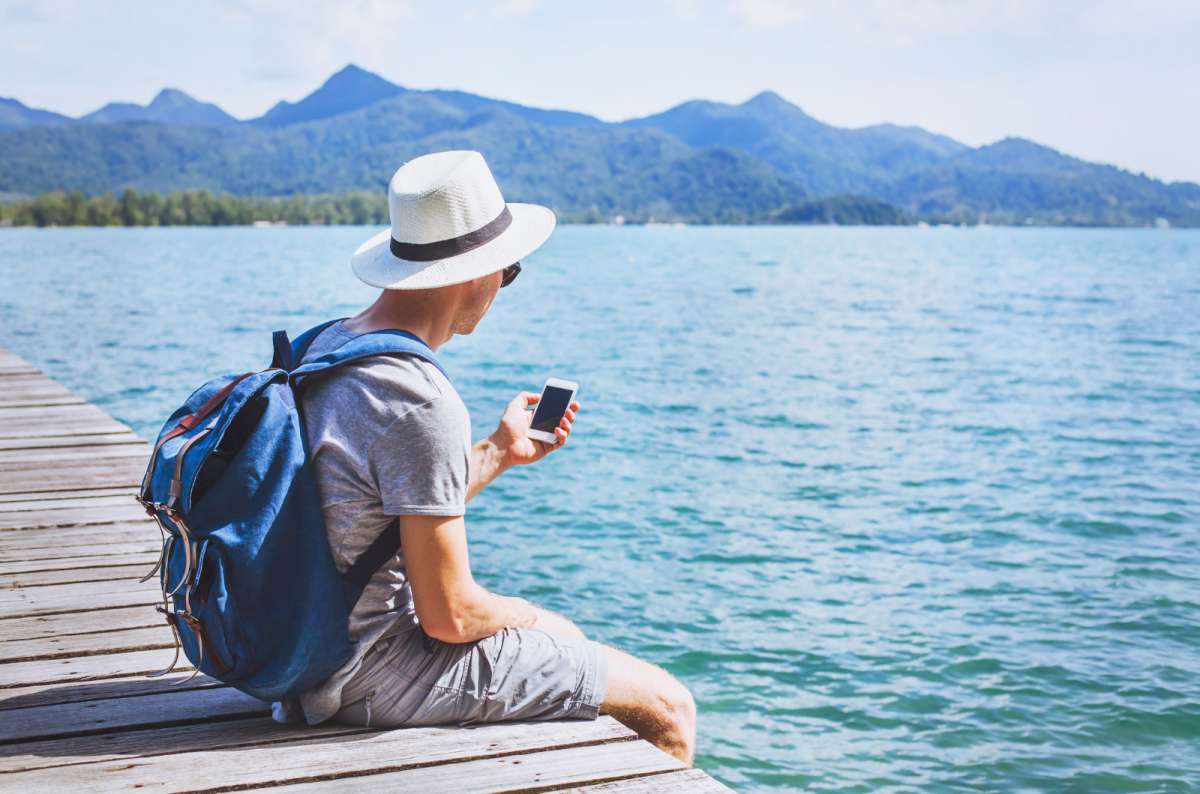a photo of a traveler checking their phone by a mountain lake