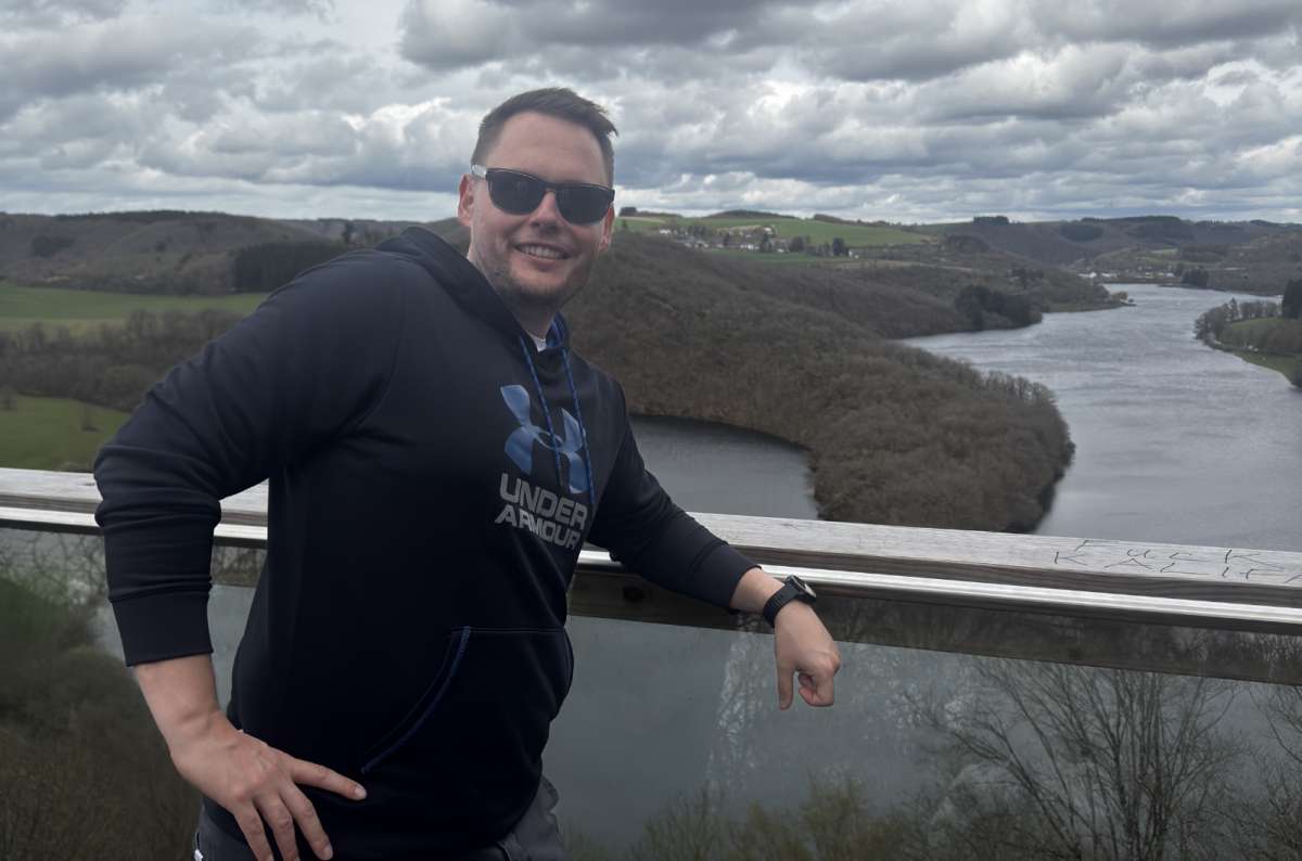 A tourist at a railing above the Upper Sûre lake and forested hills, Burfelt, Luxembourg, photo by Next Level of Travel