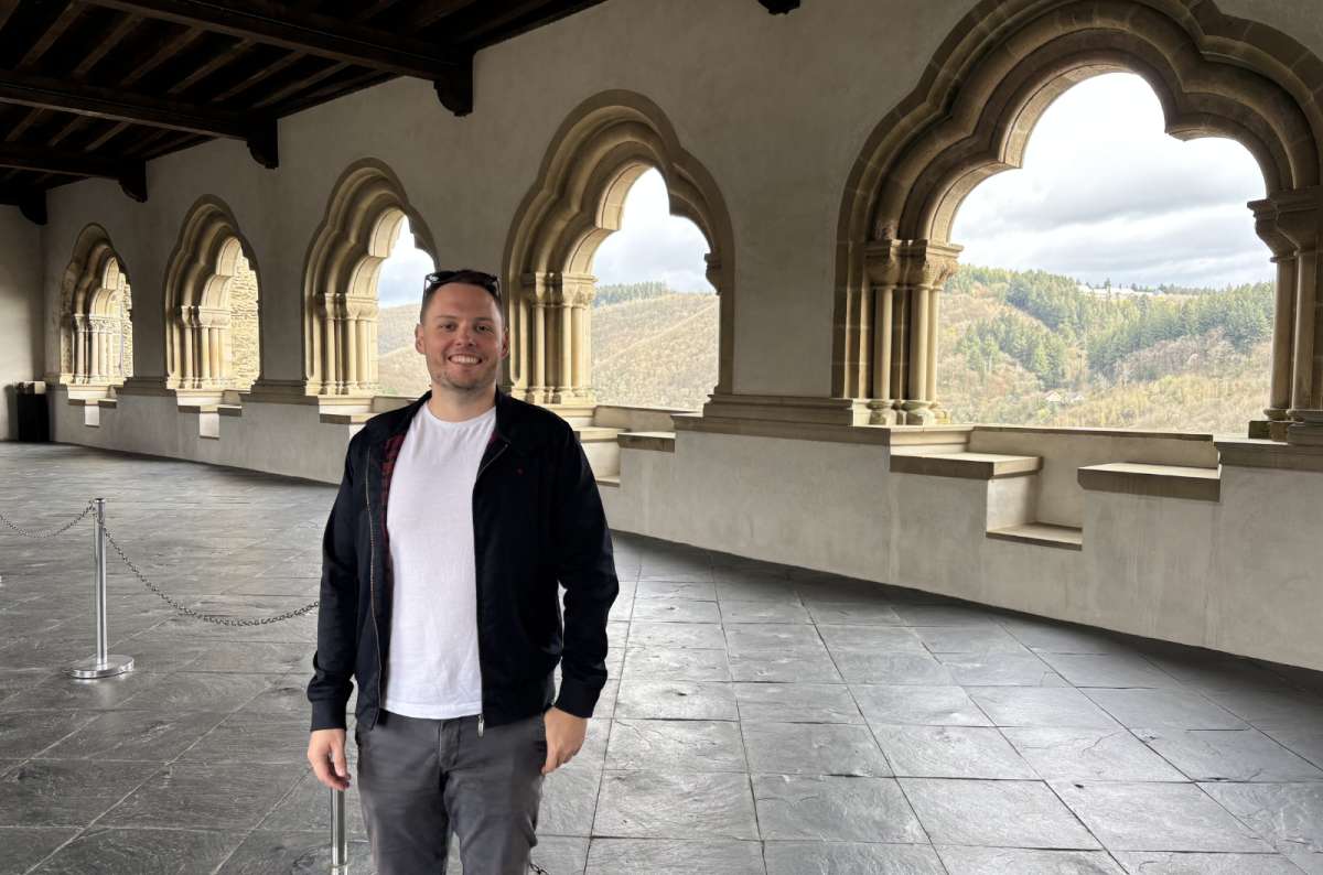 A tourist in the Gothic arched gallery inside Vianden Castle, the valley visible through the windows, Luxembourg, photo by Next Level of Travel