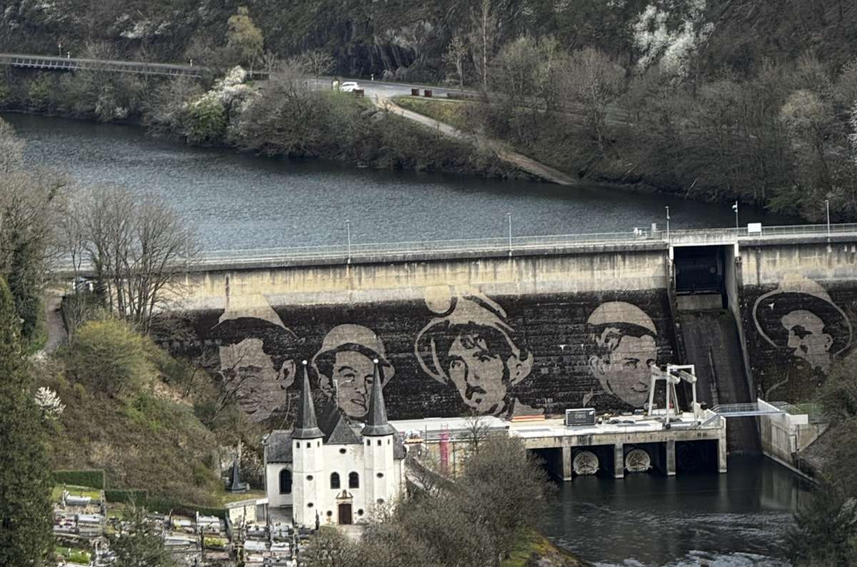 The Esch-sur-Sûre dam with its mural of faces and the white chapel below on the Sûre river, Esch-sur-Sûre, Luxembourg, photo by Next Level of Travel