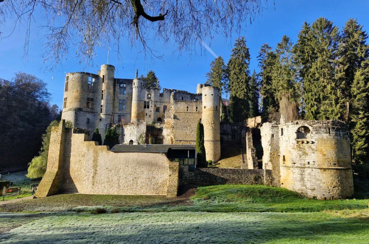 The medieval ruins of Beaufort Castle with its round towers and walls under a clear blue sky, Beaufort, Luxembourg, photo by Next Level of Travel