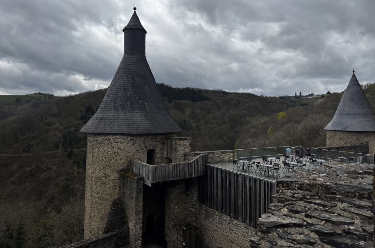 a photo of a conical slate tower and a modern wooden viewing terrace with bistro tables at Bourscheid Castle overlooking forested hills, Luxembourg, photo by Next Level of Travel