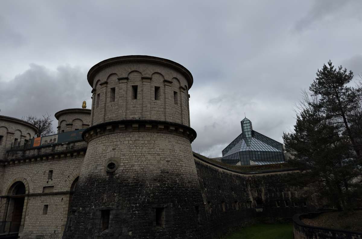 a photo of a round fortification tower of Musee Drai Eechelen with the glass pyramid of MUDAM visible behind it, Luxembourg, photo by Next Level of Travel