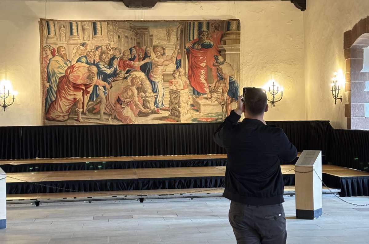 a photo of a tourist photographing a large Renaissance tapestry displayed in the great ceremonial hall of Vianden Castle, Luxembourg, photo by Next Level of Travel
