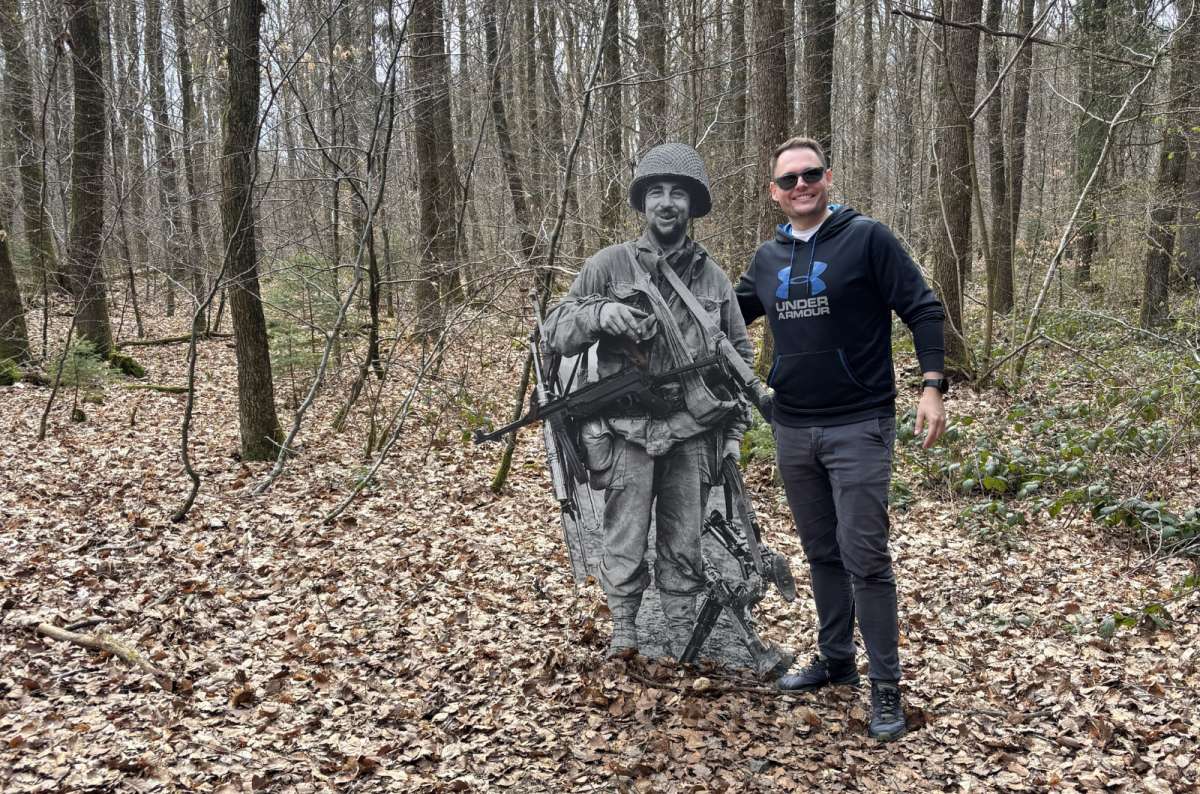 a photo of a tourist posing next to a life-size photographic cutout of a WWII soldier on the Schumannseck Memorial Trail, Luxembourg, photo by Next Level of Travel