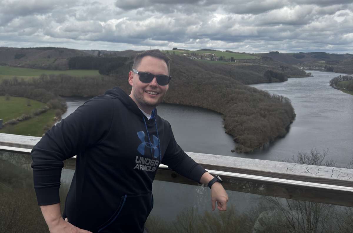 a photo of a tourist smiling at a viewpoint overlooking a dramatic river meander in the Luxembourg Ardennes, photo by Next Level of Travel