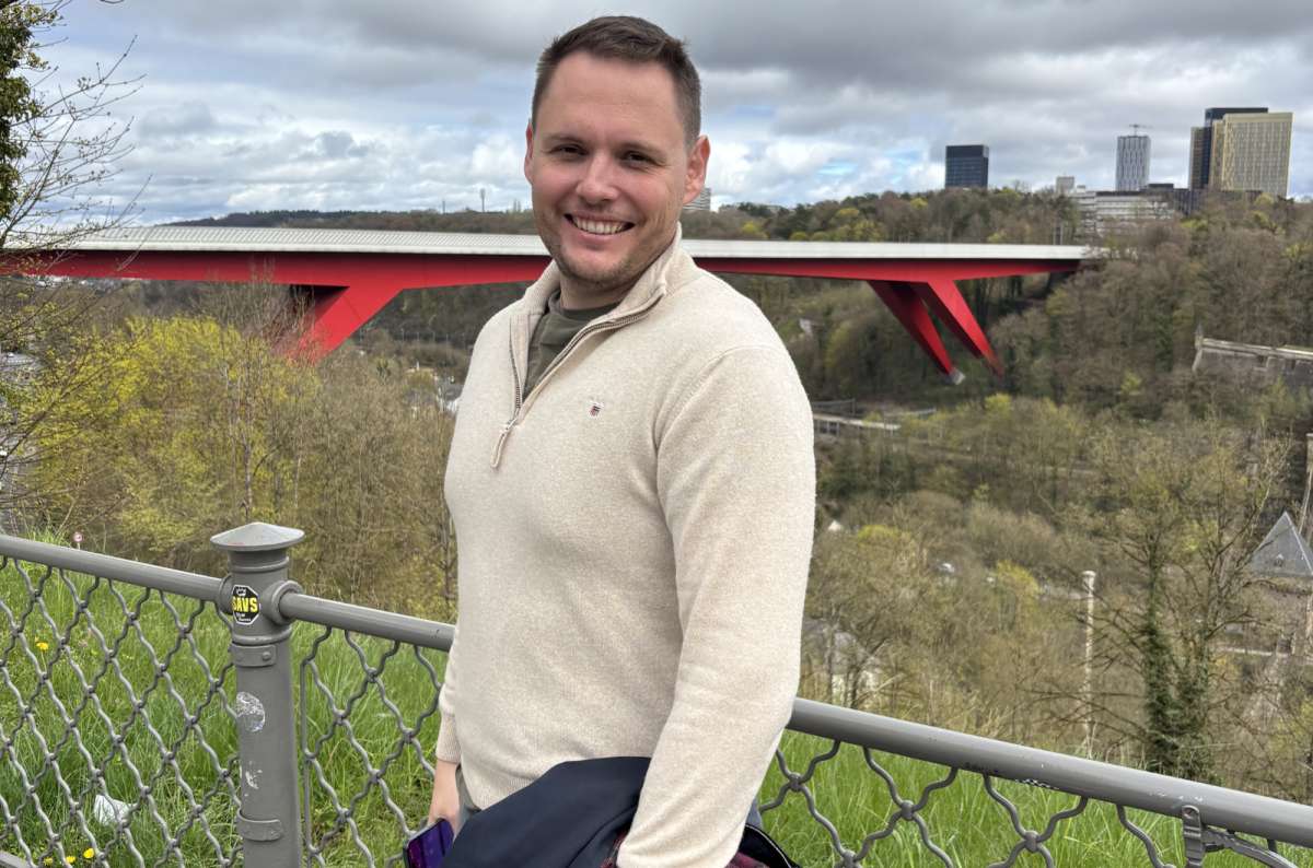 a photo of a tourist smiling in front of the Grande-Duchesse Charlotte Bridge spanning the Alzette Valley, Luxembourg City, photo by Next Level of Travel