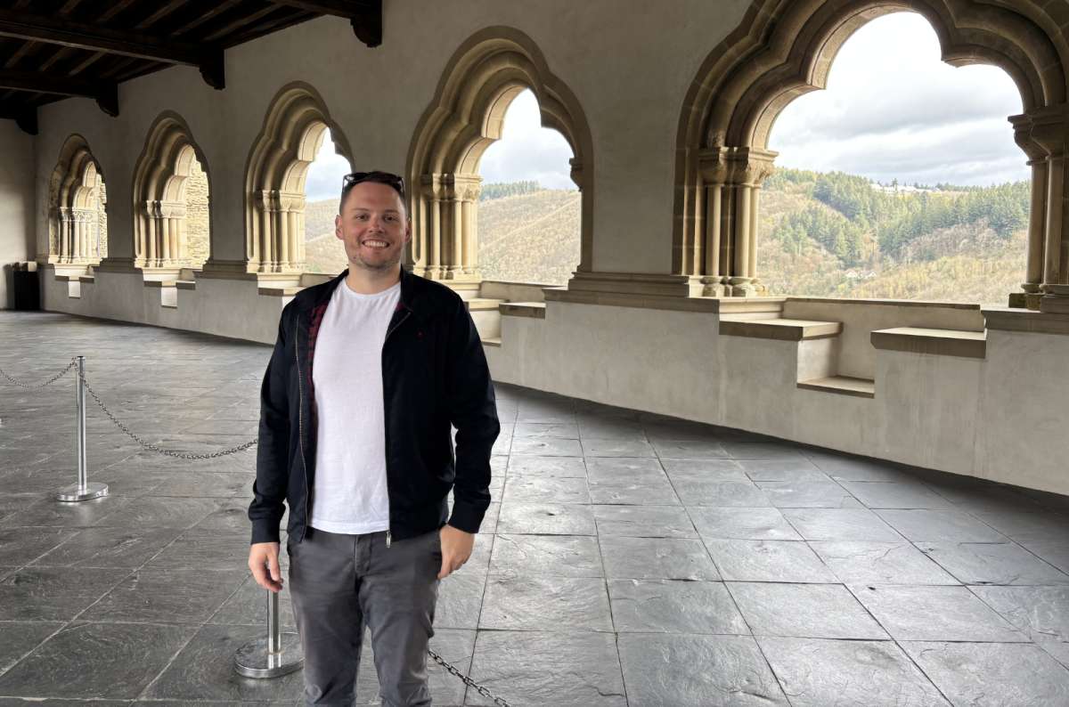a photo of a tourist standing in the monumental gallery of Vianden Castle, looking through a row of arched windows, Luxembourg, photo by Next Level of Travel