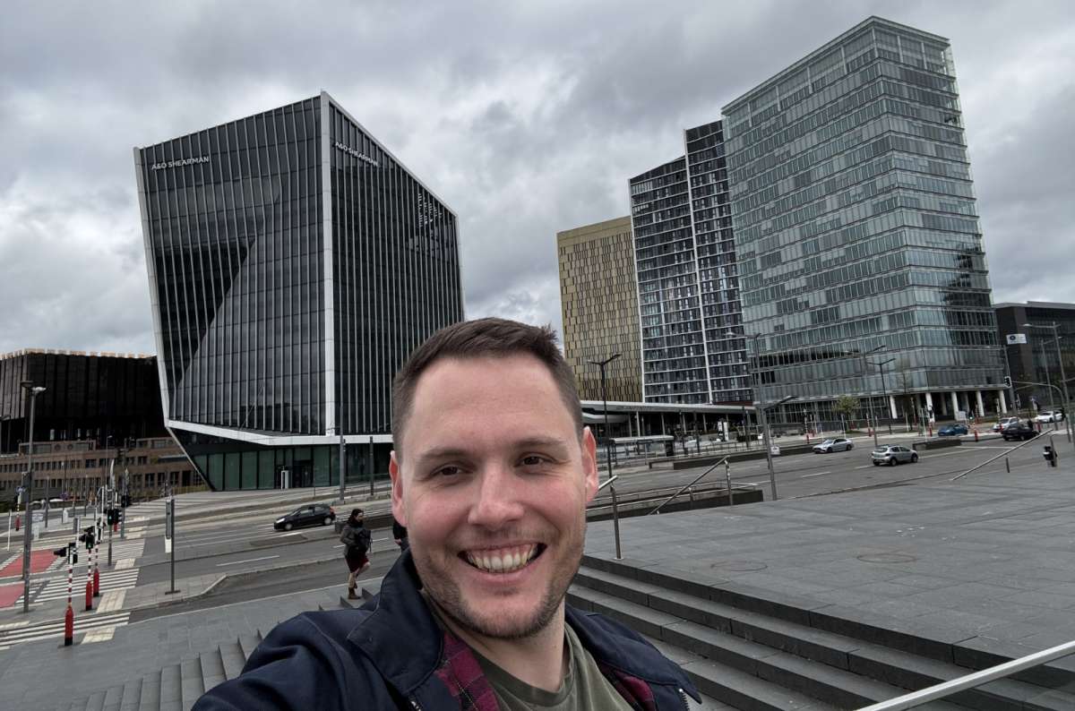 a photo of a tourist taking a selfie in front of the modern glass office towers of the Kirchberg financial district in Luxembourg City, Luxembourg, photo by Next Level of Travel