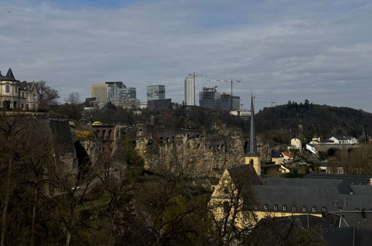 a photo of a view of Luxembourg City showing the old town cliff with the Bock Casemates carved into the rock, the Neumunster, and the Kirchberg skyline in the background, photo by Next Level of Travel