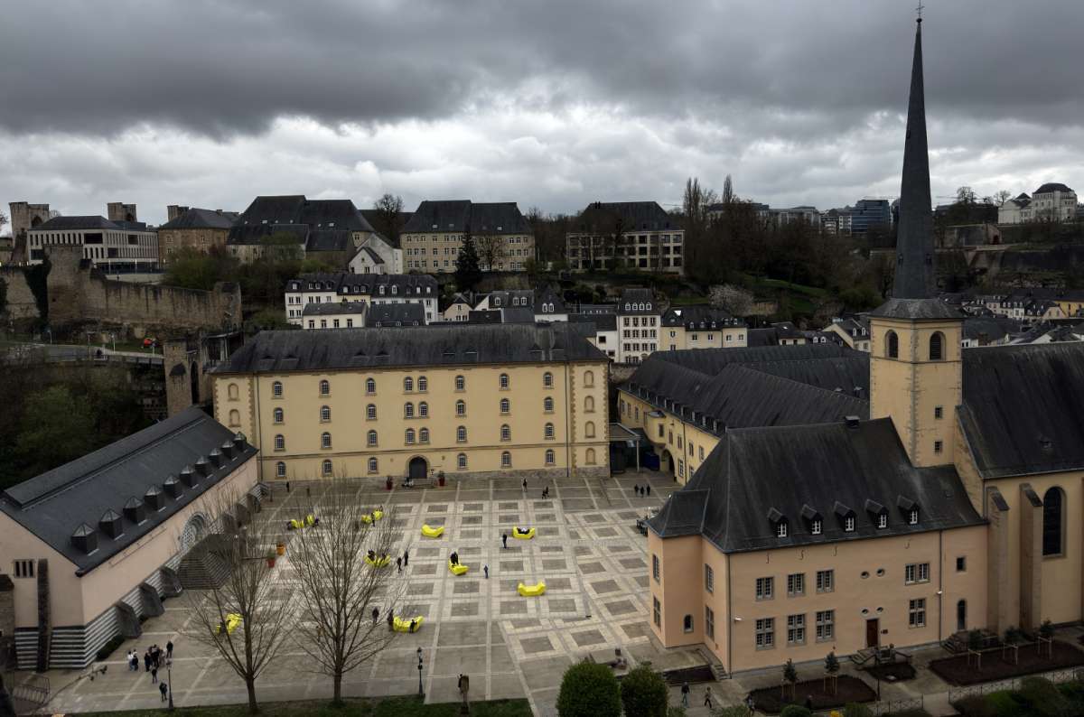 a photo of the Neumunster Abbey courtyard with yellow art sculptures scattered across the square and the abbey church rising above, Luxembourg, photo by Next Level of Travel
