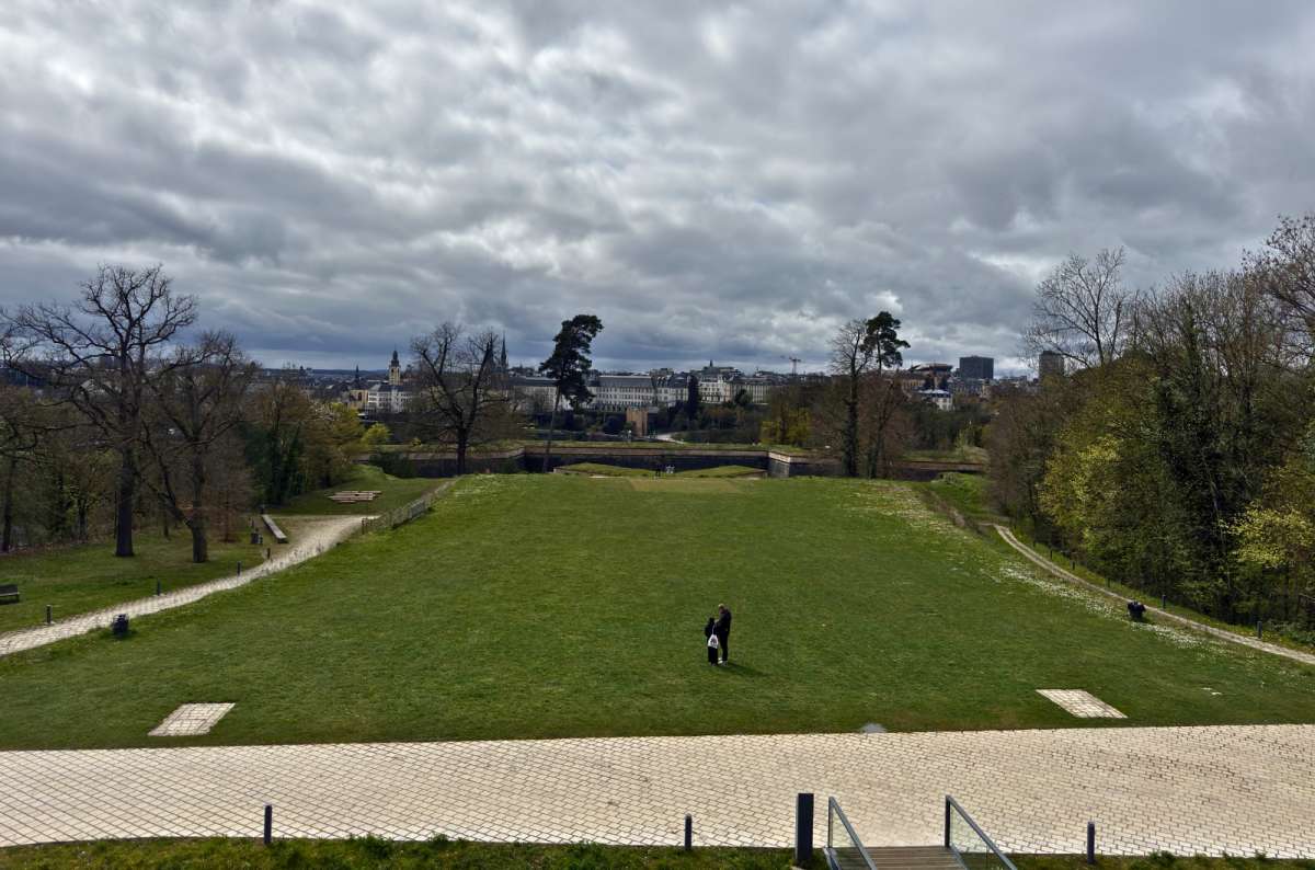 a photo of the wide green esplanade with a lone visitor standing on the path, and the Luxembourg skyline, Luxembourg, photo by Next Level of Travel