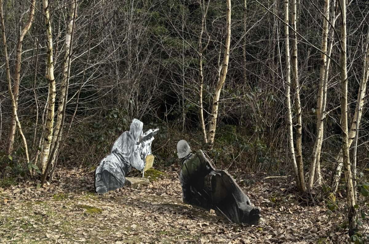a photo of two figures of WWII soldiers in winter camouflage capes crouching in a bare winter forest, Schumannseck WWII trail, Luxembourg, photo by Next Level of Travel