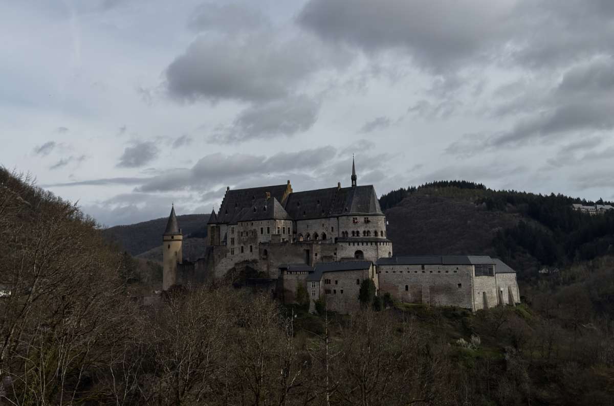 a photo of Vianden Castle rising above the forested hillside on a dramatic overcast day, Luxembourg, photo by Next Level of Travel