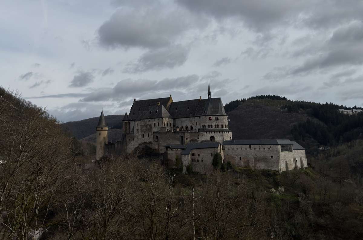 a photo of Vianden Castle rising above the forested hillside on a dramatic overcast day, Luxembourg, photo by Next Level of Travel