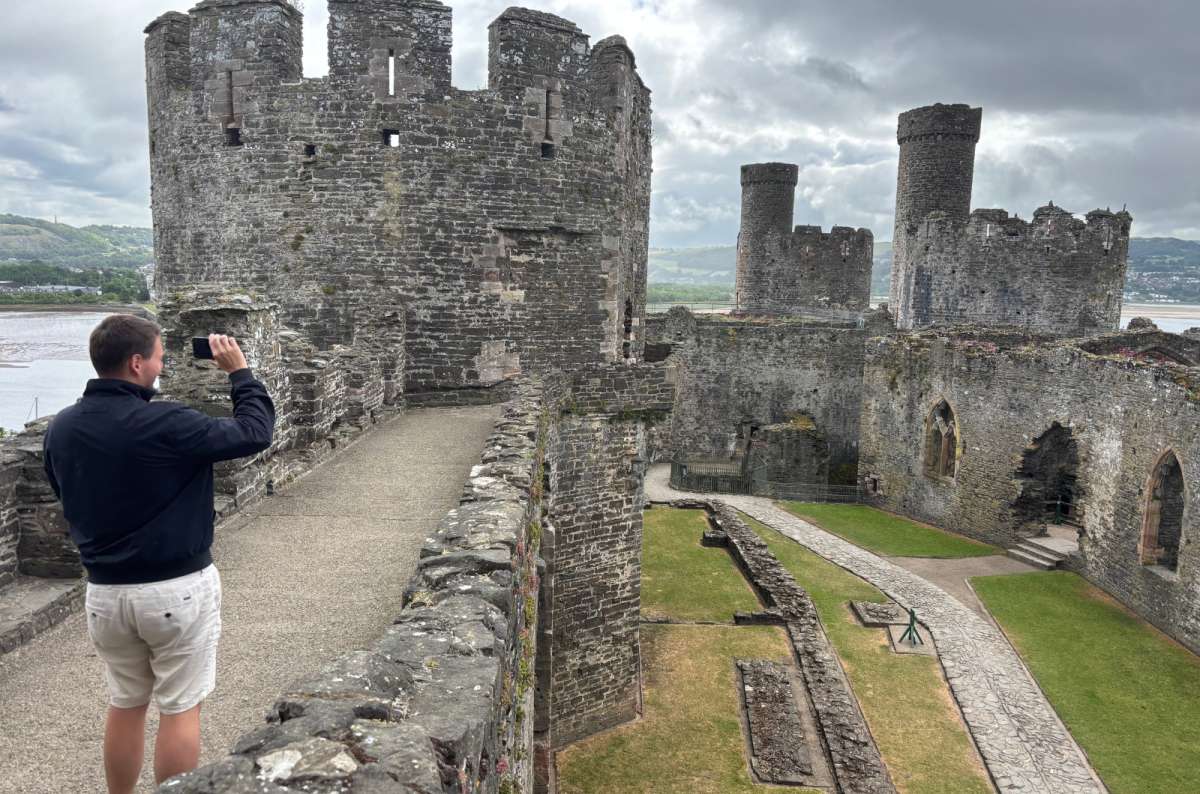 a photo of a tourist photographing the towers and ruined great hall of Conwy Castle above the estuary, Conwy, Wales, photo by Next Level of Travel