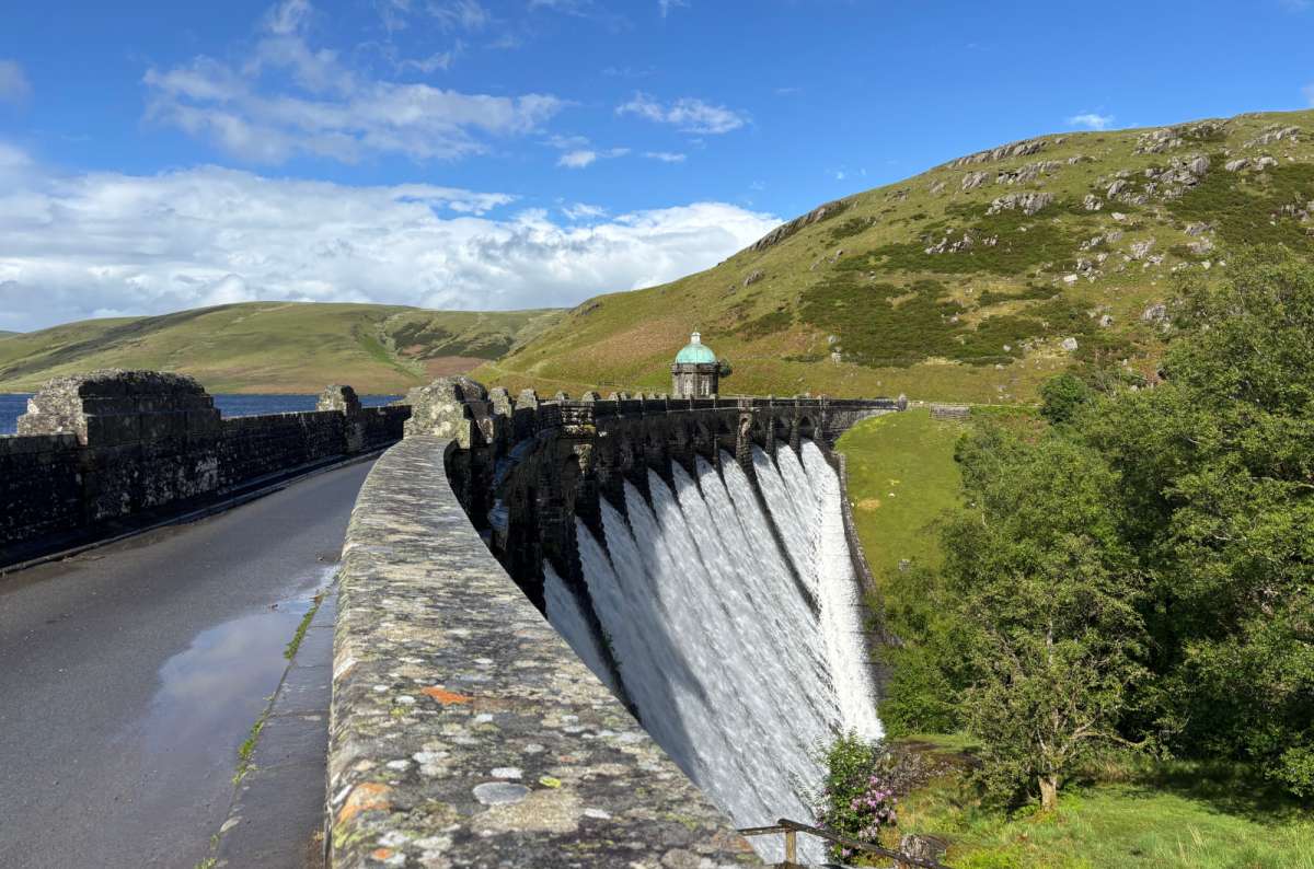 a photo of a tourist's view along the top of Craig Goch dam as water spills over the edge, Elan Valley, Wales, photo by Next Level of Travel