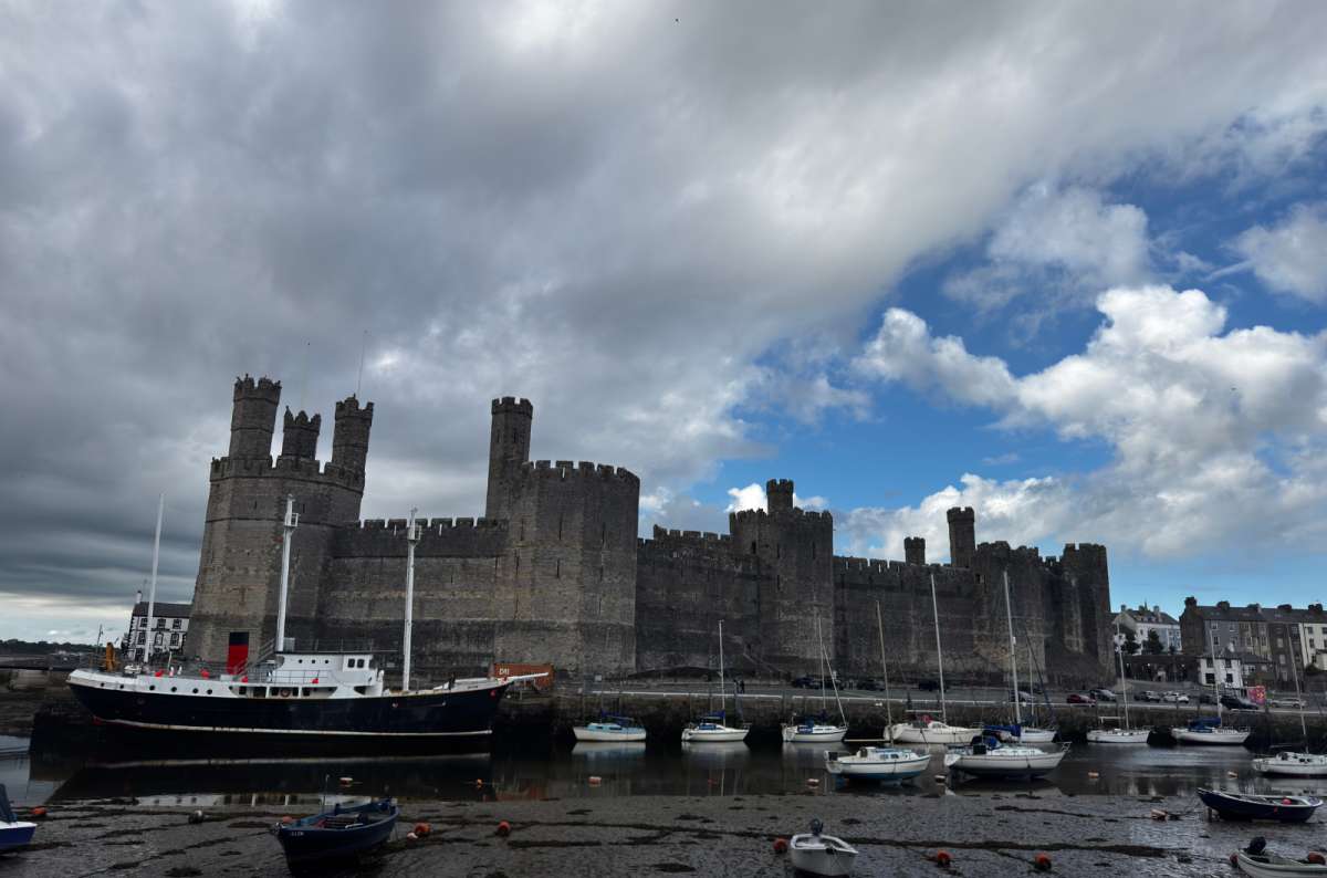 a photo of Caernarfon Castle rising above the harbour and moored boats under a moody sky, Caernarfon, Wales, photo by Next Level of Travel