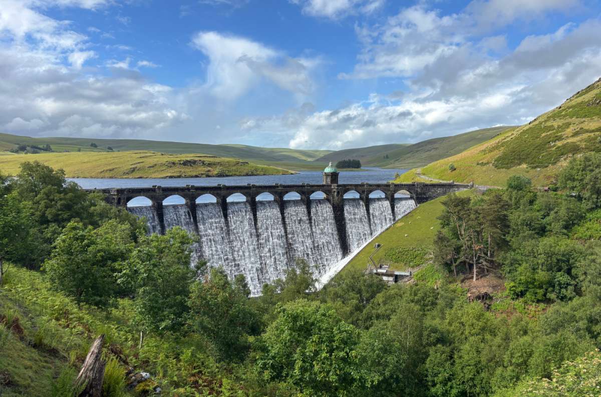 a photo of water cascading over the arches of Craig Goch dam with the reservoir and hills behind, Elan Valley, Wales, photo by Next Level of Travel