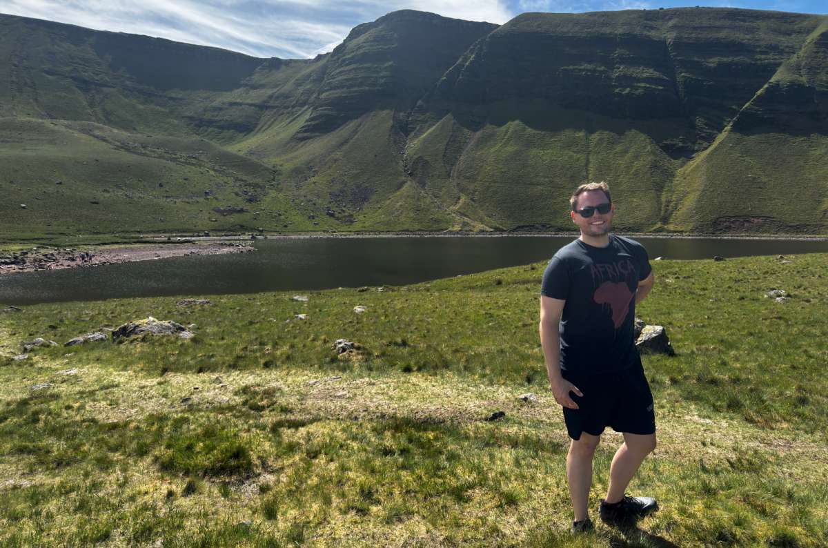 a torusit posing on a hike, surrounded by mountains, grass and lakes in Brecon Beacons, Wales, photo by Next Level of Travel