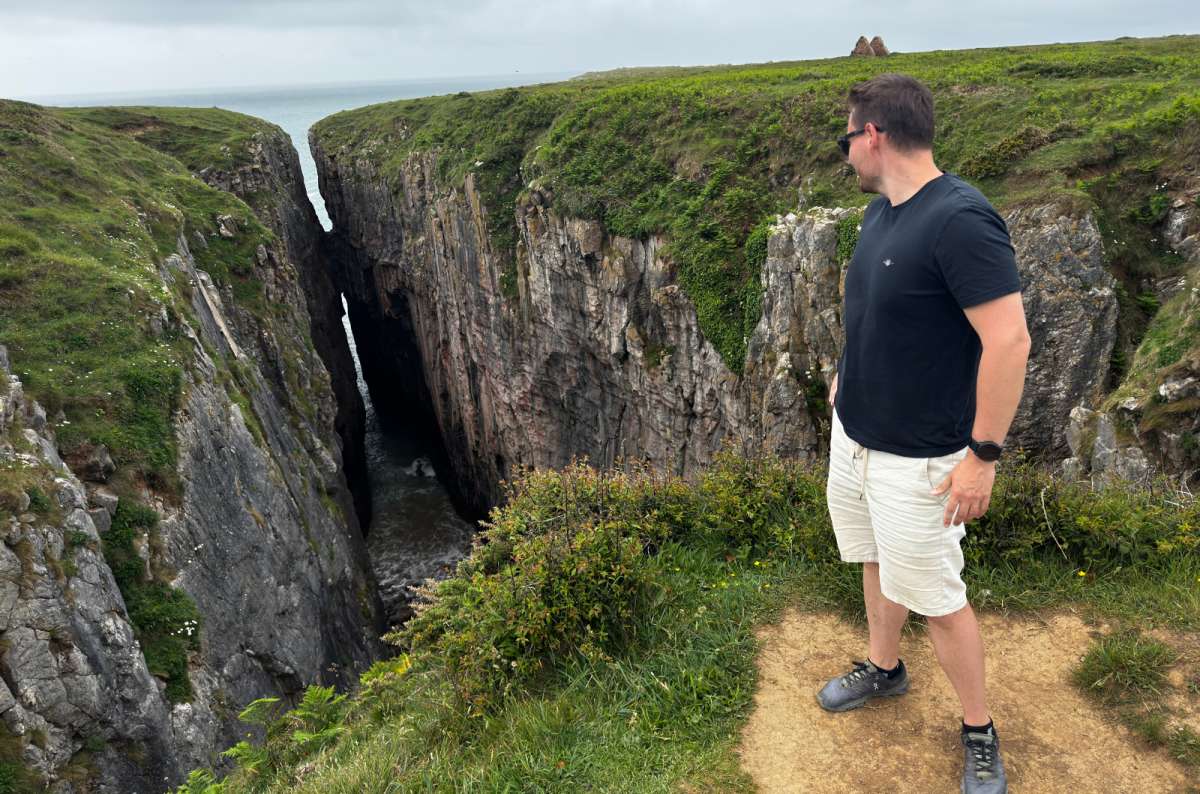 a photo of a tourist looking into the deep cliff chasm of Huntsman's Leap on the coast near St Govan's Chapel, Pembrokeshire, Wales, photo by Next Level of Travel