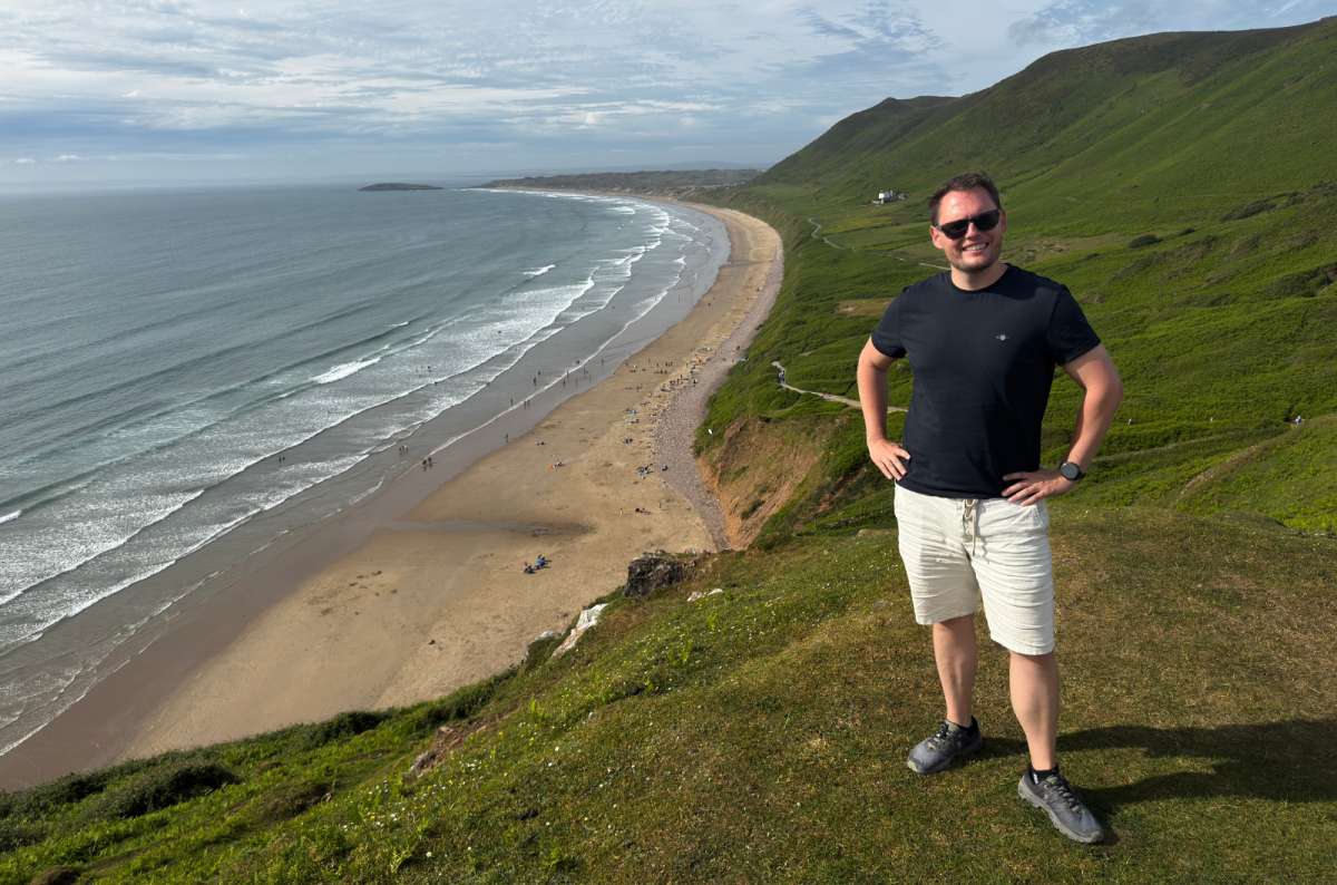 a photo of a tourist on the clifftop above the vast sweeping sands of Rhossili Bay, Gower Peninsula, Wales, photo by Next Level of Travel