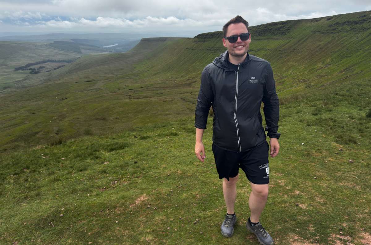 a photo of a tourist on the grassy ridge of Pen y Fan above rolling green valleys, Bannau Brycheiniog, Wales, photo by Next Level of Travel