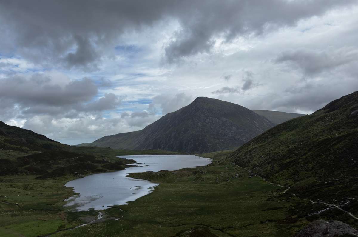 a photo of Llyn Idwal below the dark cliffs and peak of Glyder Fawr under moody clouds, Eryri National Park, Wales, photo by Next Level of Travel