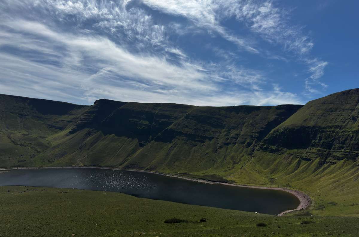 a photo of Llyn y Fan Fach ringed by steep dramatic slopes under a blue sky, Bannau Brycheiniog, Wales, photo by Next Level of Travel