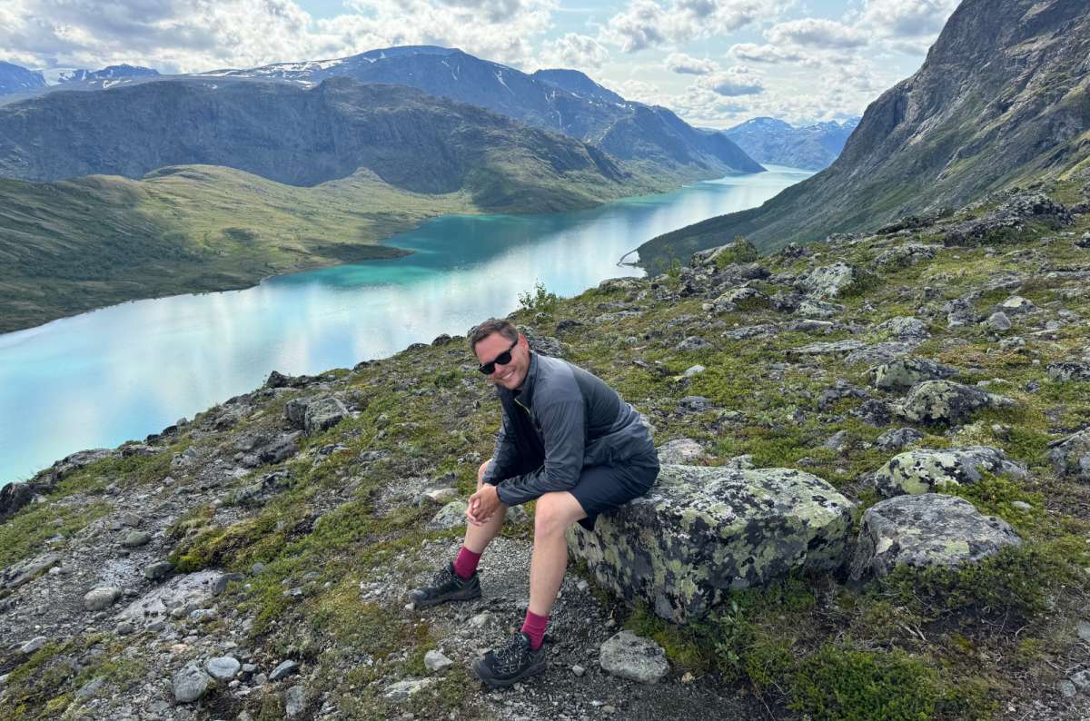 a photo of a tourist sitting on a rock overlooking Gjende and Bessvatnet lakes on the Besseggen ridge, Jotunheimen National Park, Norway, photo by Next Level of Travel