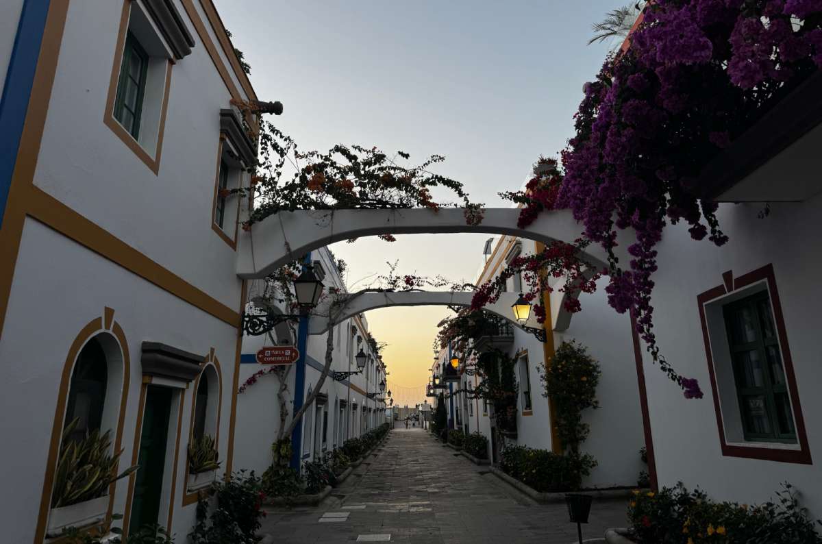 a photo of a narrow whitewashed lane framed by flowering bougainvillea arches at sunset, Puerto de Mogán, Canary Islands, photo by Next Level of Travel
